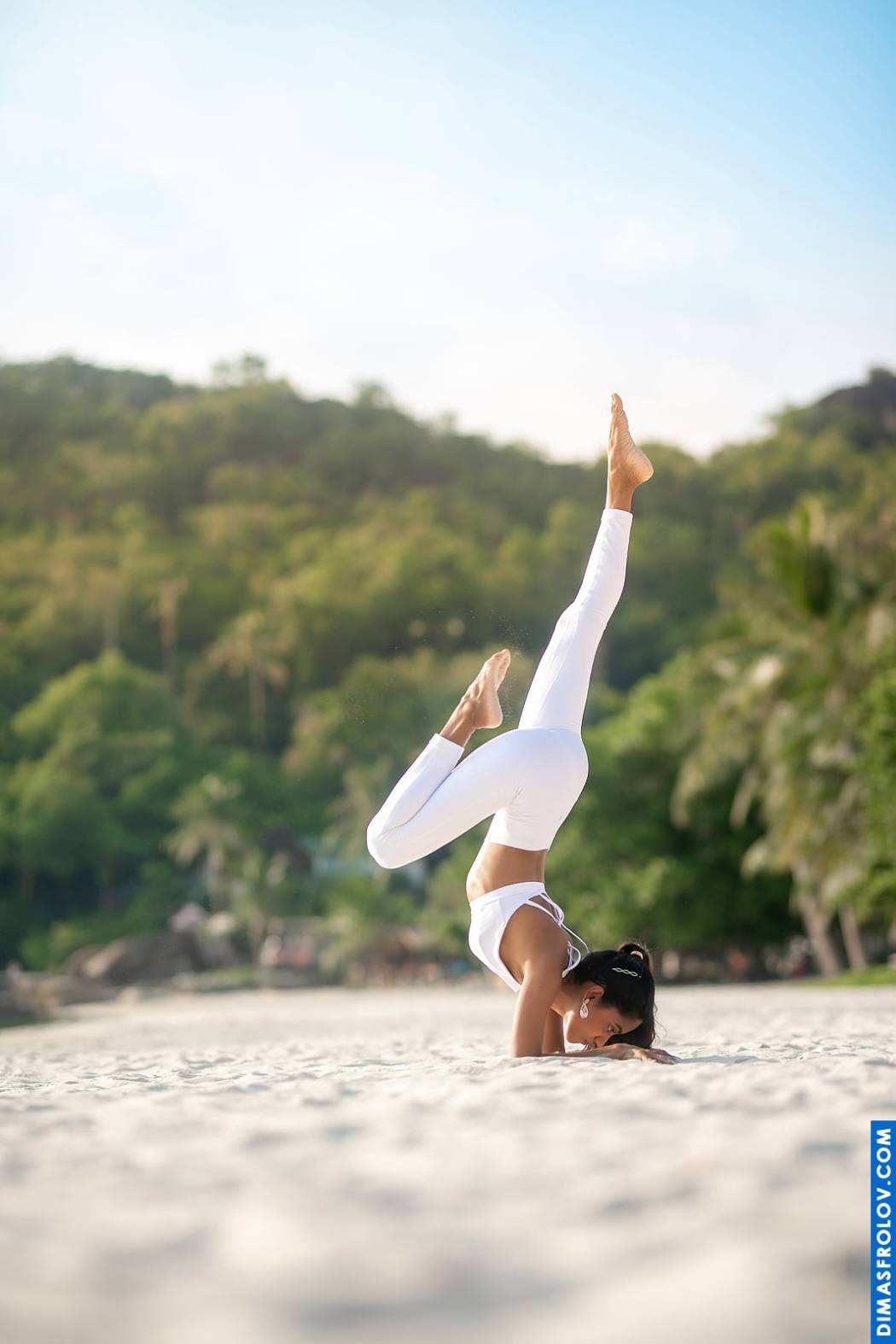 Elegant yoga balance: woman in white performing a handstand variation on the beach