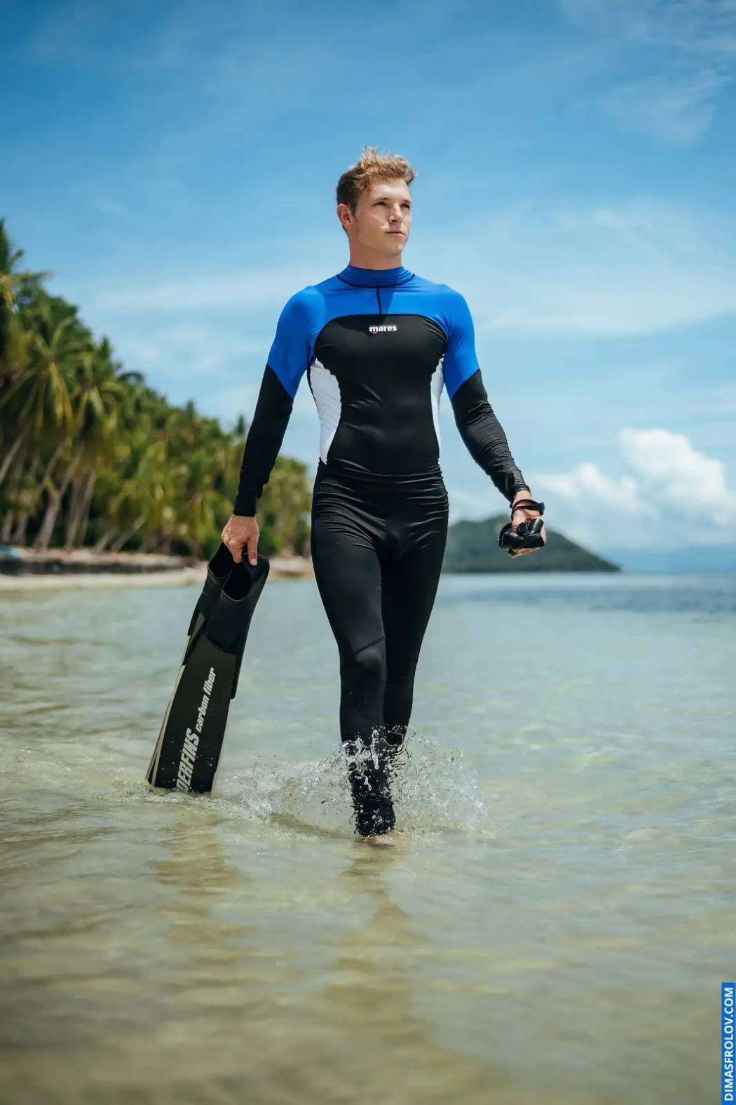 Diver walking out of the ocean in wetsuit with fins in tropical setting