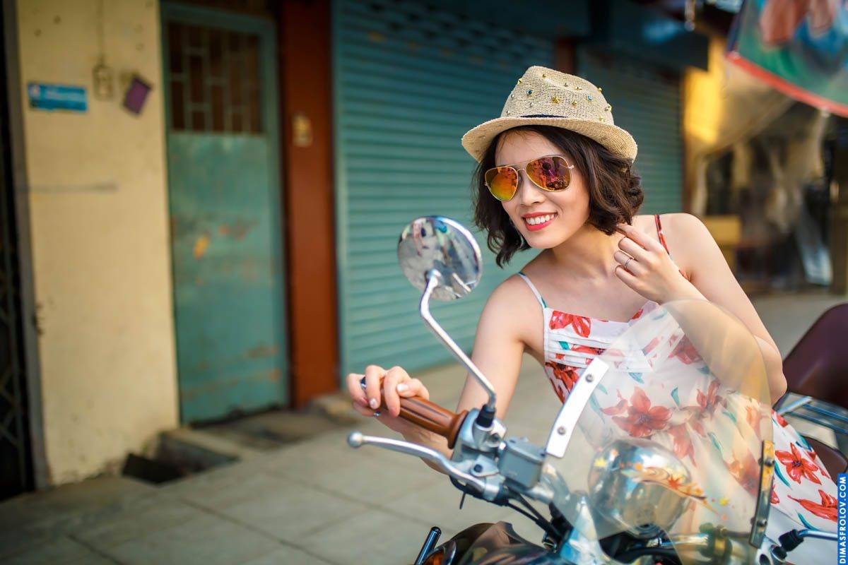 Travel-style portrait of a stylish woman in a floral dress with hat and sunglasses on scooter