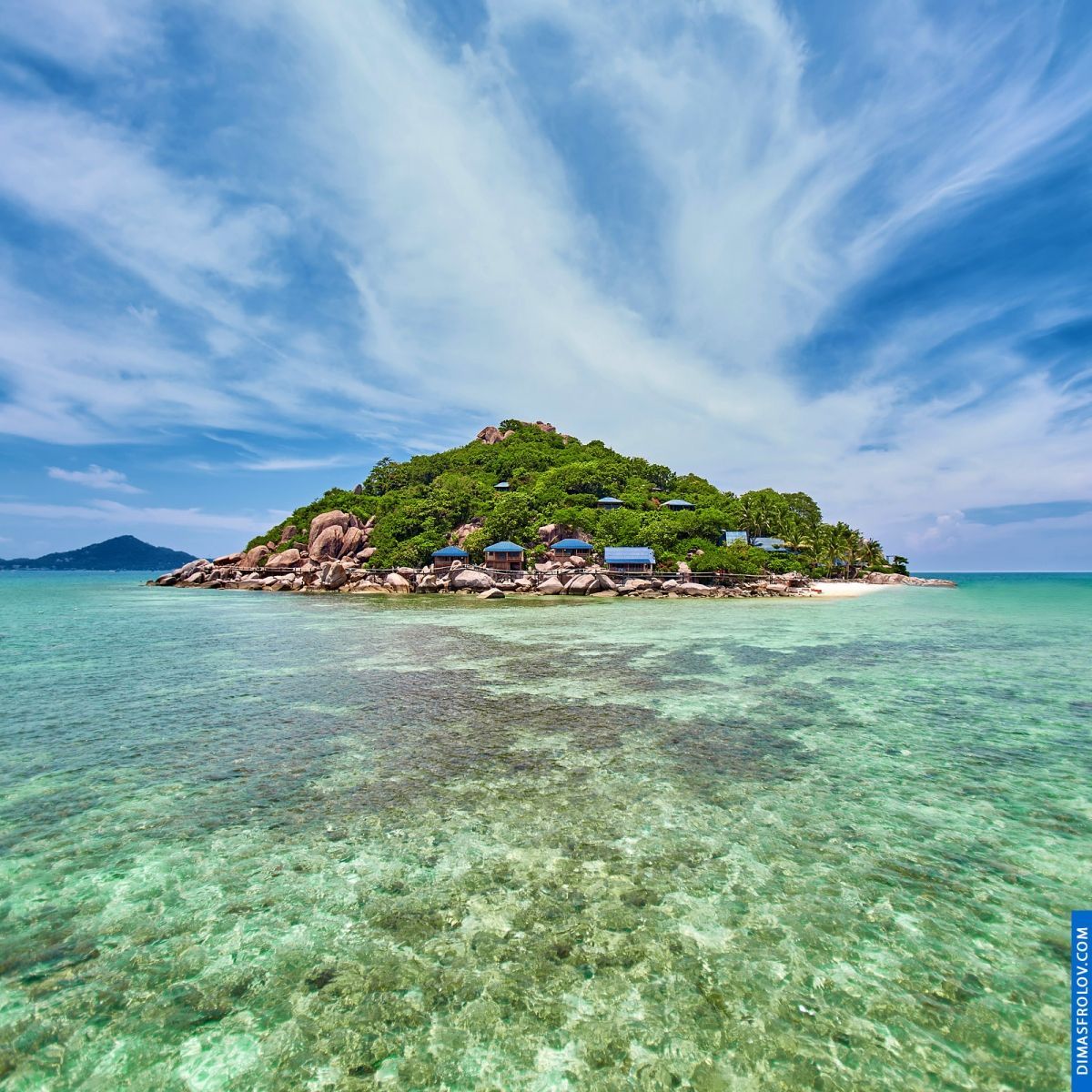Small tropical island with lush green vegetation surrounded by clear turquoise water and coral reefs
