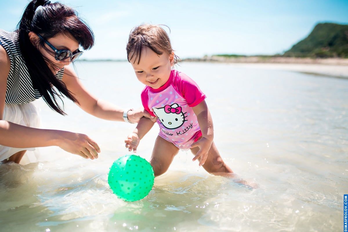 Sessão de fotos na praia com crianças — menina brincando na água rasa com a mãe