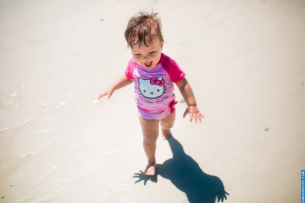Foto espontânea na praia — criança pequena correndo na areia com um maiô da Hello Kitty
