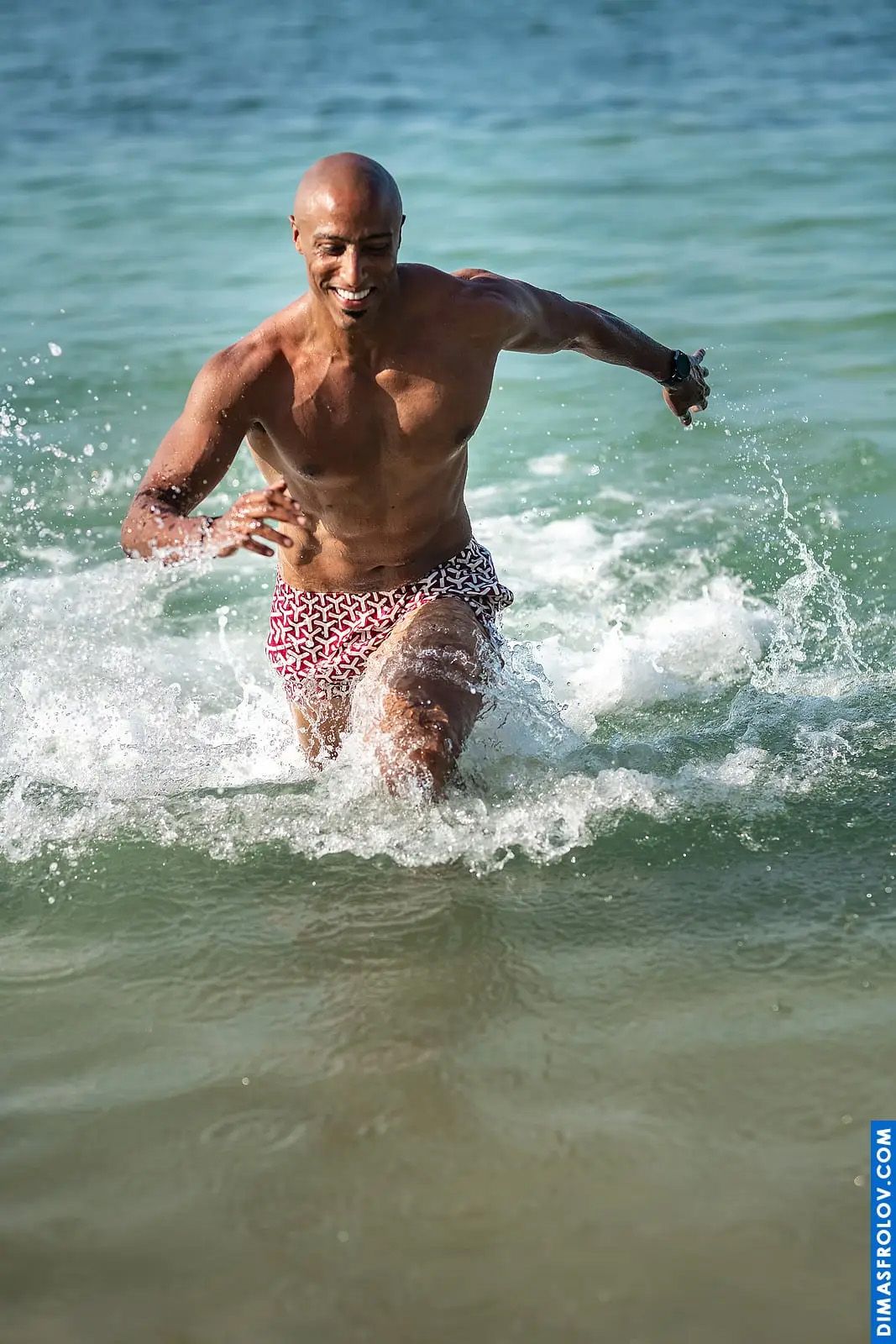 Action beach photo of muscular man running through ocean waves