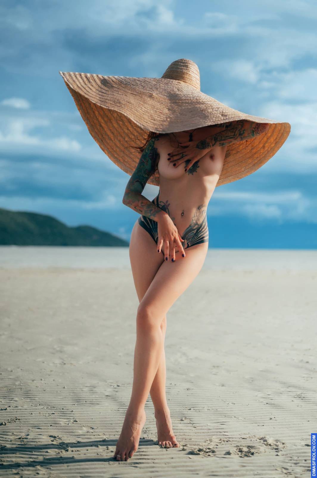 Stylish nude photo with woman in big straw hat on tropical beach
