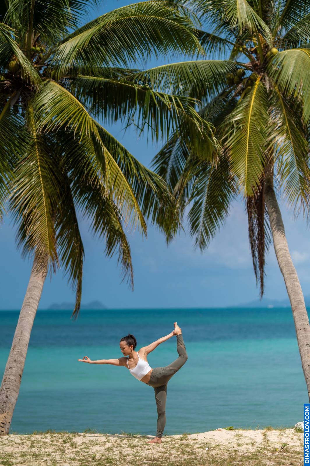Yoga pose on tropical beach between palm trees with turquoise sea in background