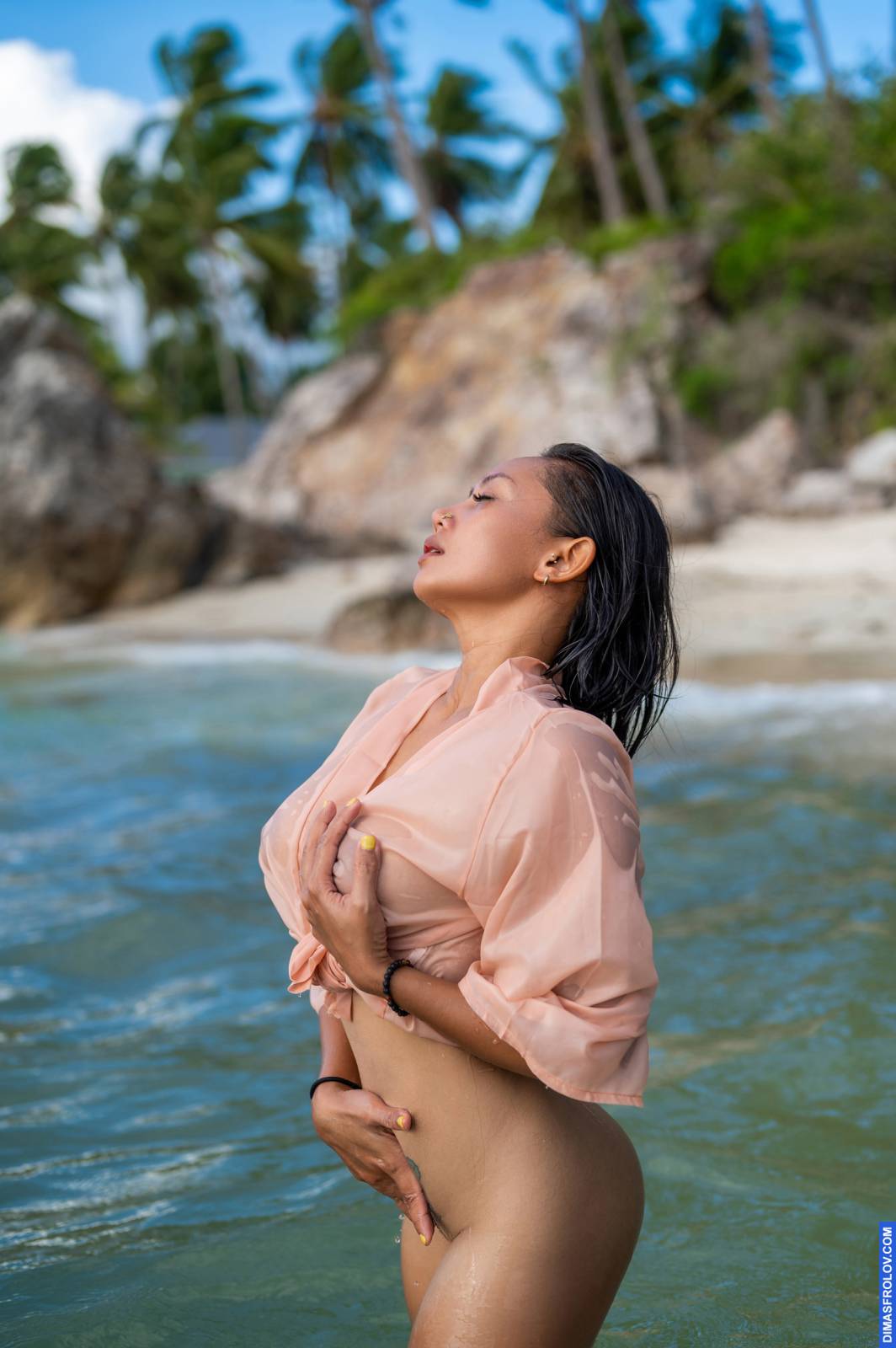 Mulher sem blusa em camisa translúcida de pé no mar tropical