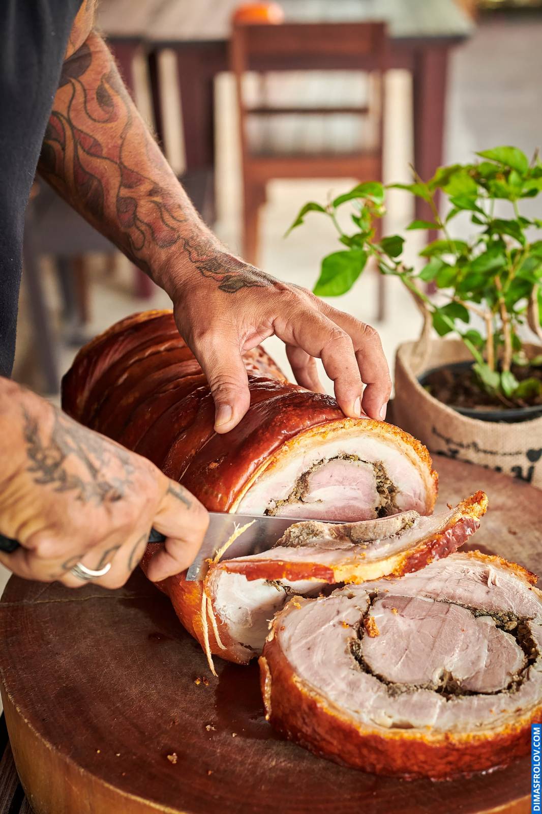 Naturally lit, life-style shot of tattooed hands slicing porchetta on a wooden board, capturing a real cooking moment perfect for food bloggers and restaurants showcasing their preparation