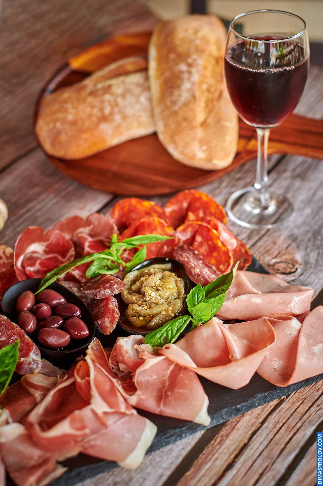 Naturally lit, life-style shot of a charcuterie board with various cured meats, cheese, and bread, served with a glass of red wine, perfect for restaurants and wine bars showcasing their pairings