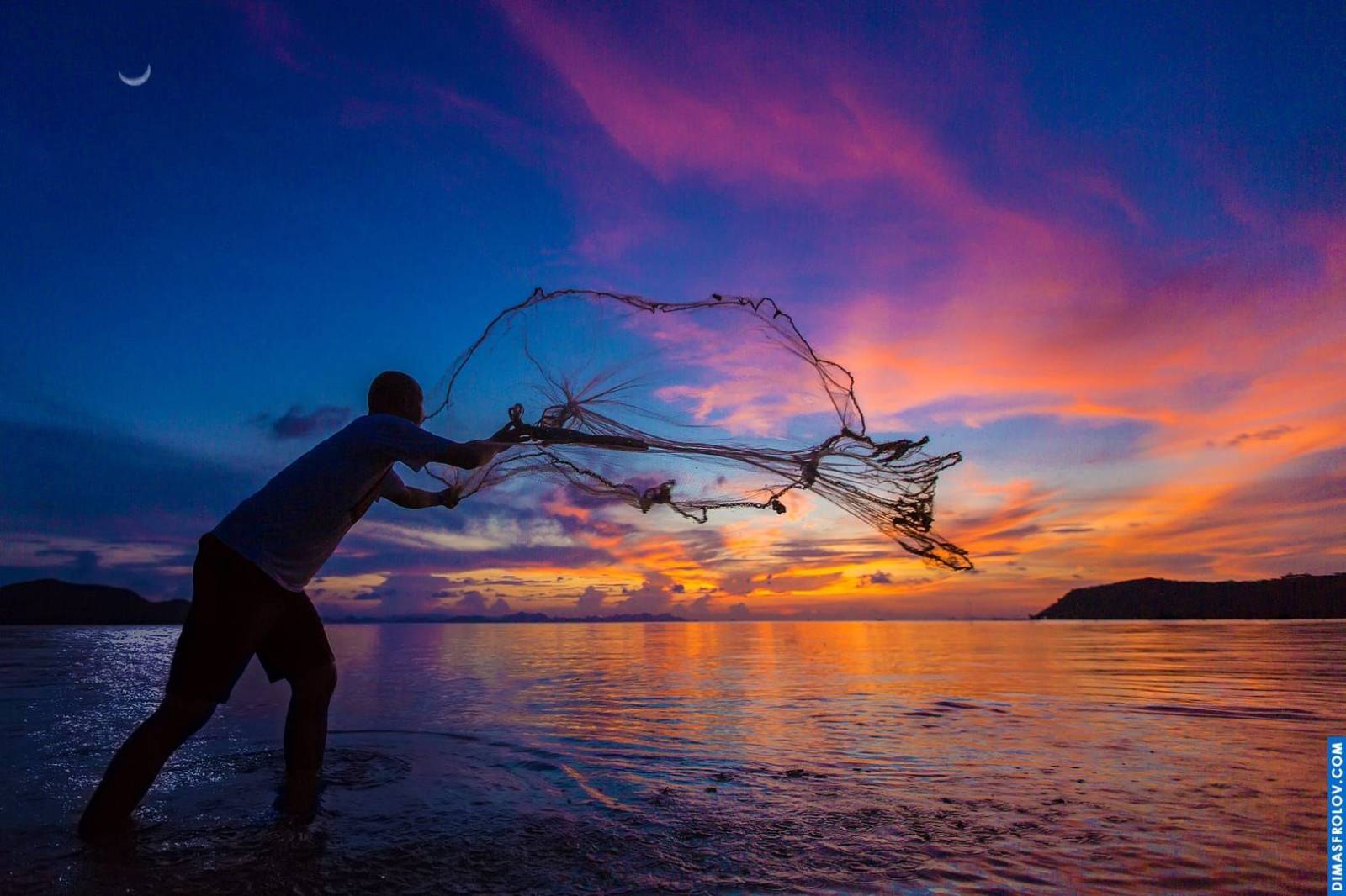 Silhouette of a person fishing at sunset with vibrant orange and purple hues reflecting on the calm water