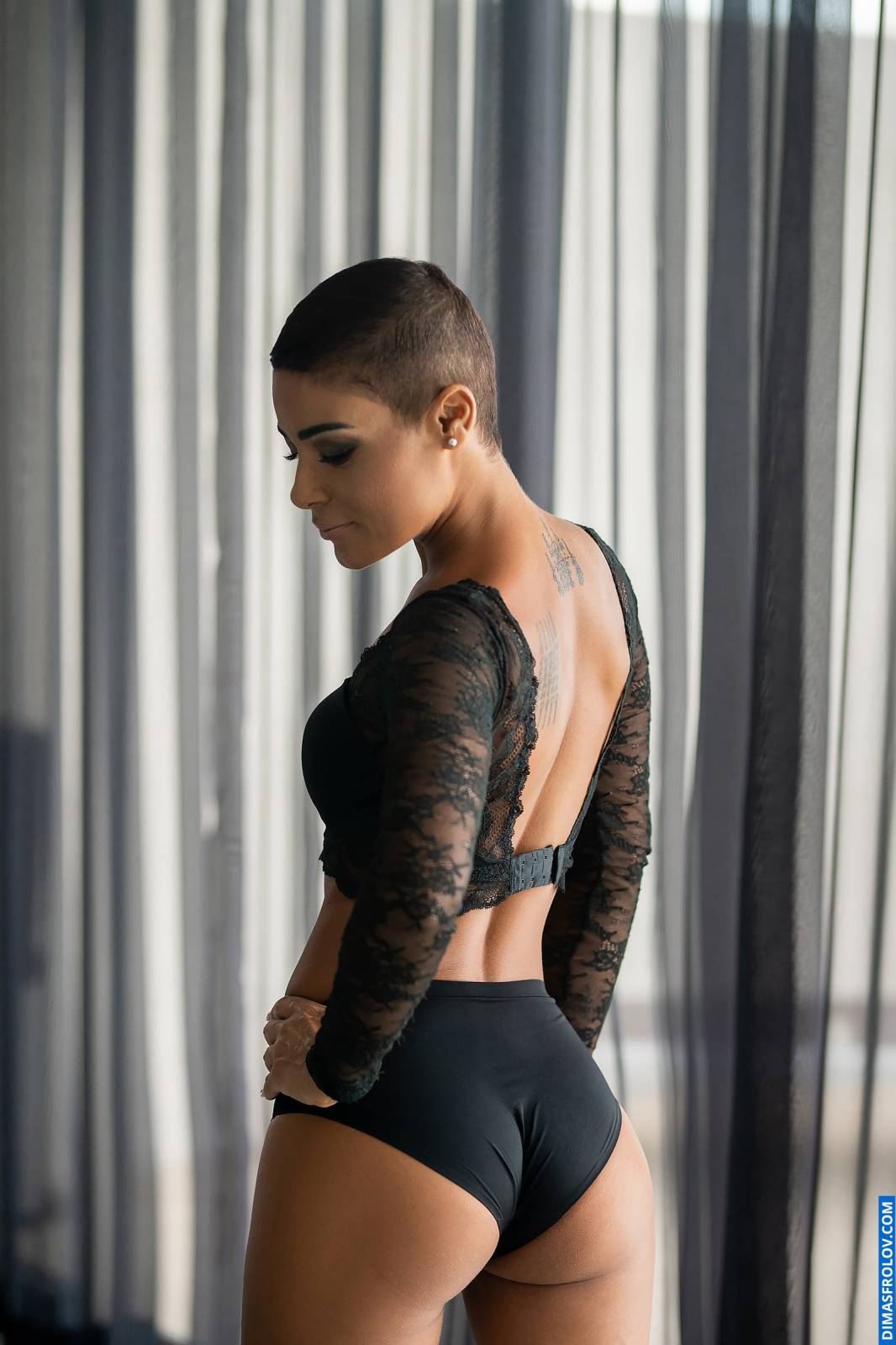 Retrato editorial boudoir de uma mulher em um body de renda transparente ao lado de cortinas