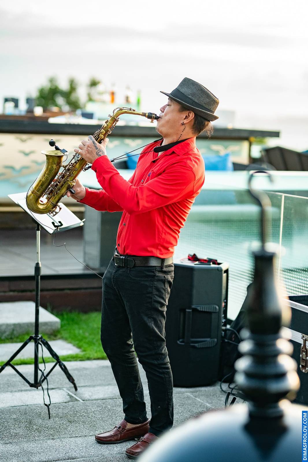Live saxophone performance at outdoor event — musician in red shirt playing at sunset