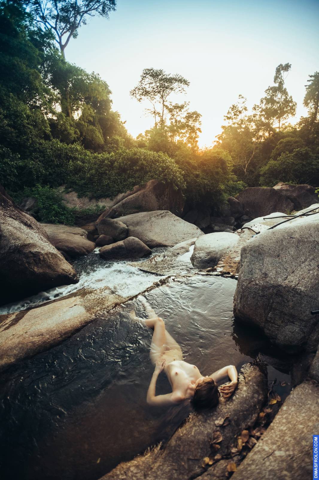 Foto artística de nu feminino flutuando em um riacho de montanha ao pôr do sol