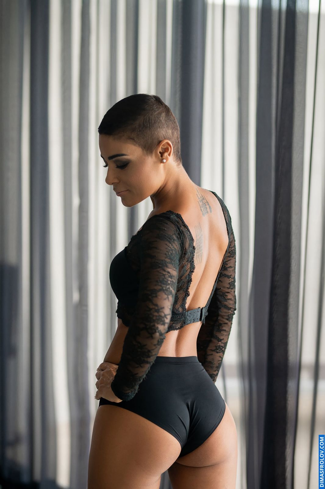 Editorial boudoir portrait of a woman in sheer lace bodysuit by curtains