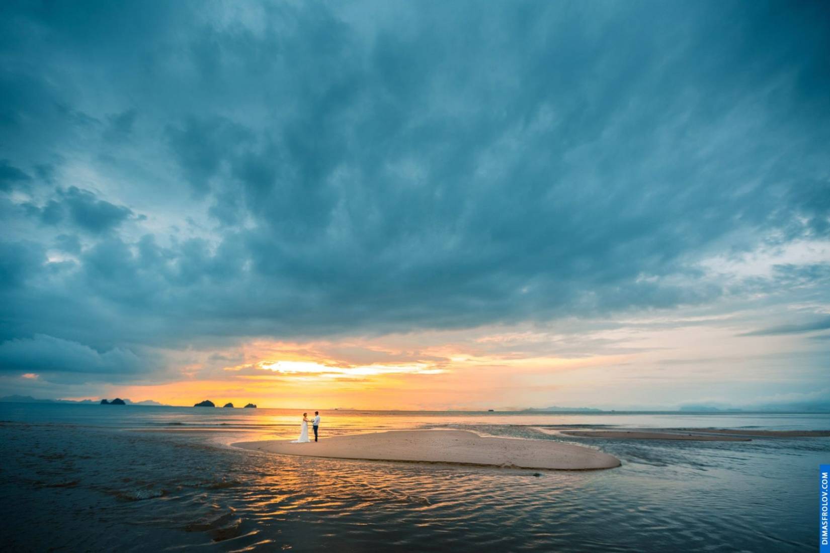 คู่แต่งงานยืนบนเกาะทรายรูปหัวใจใต้ท้องฟ้าสวยงาม