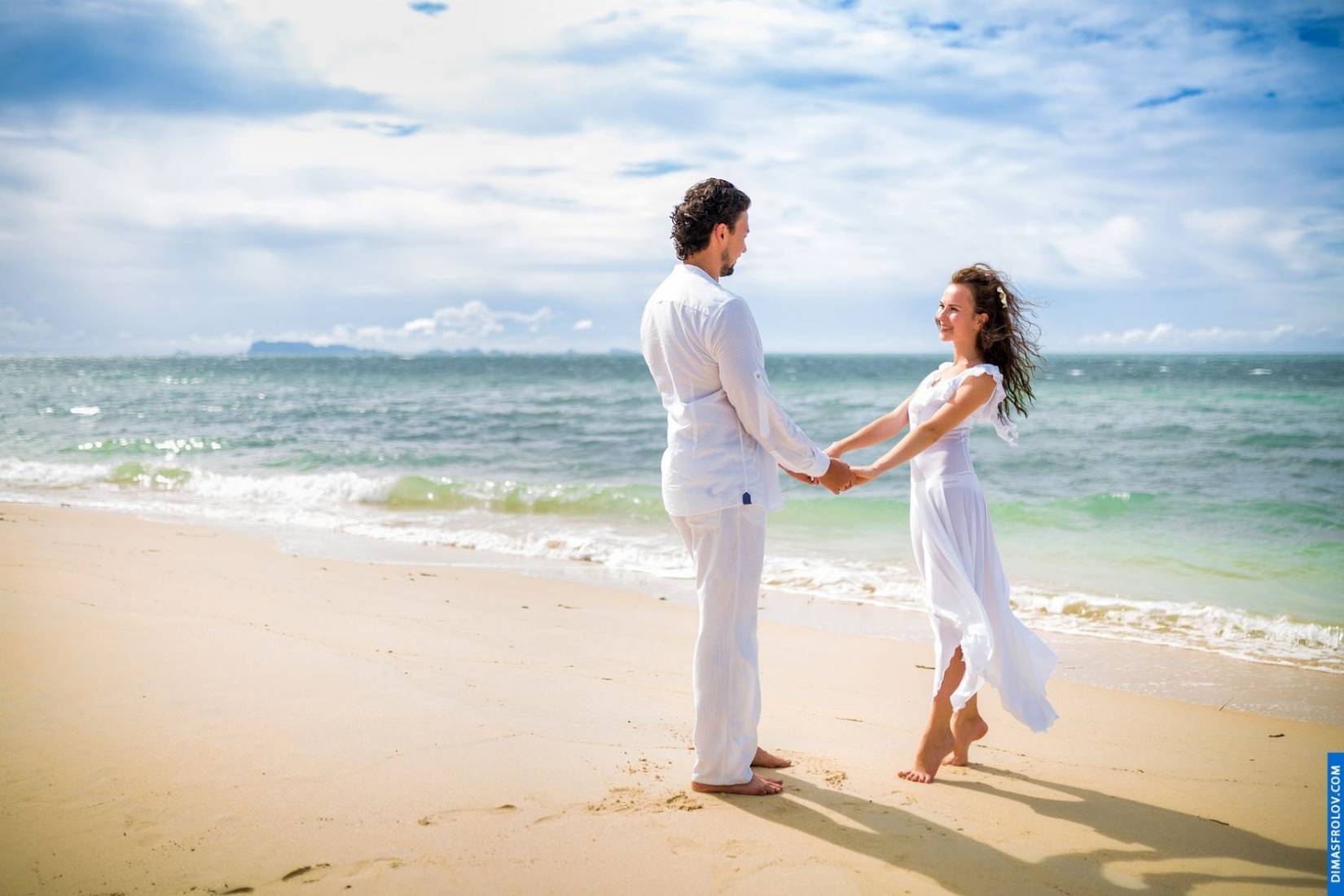 Playful moment on the beach with couple dancing in white outfits