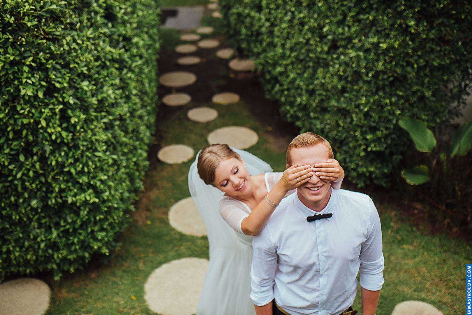Playful bride surprises groom among garden hedges — fun and candid moment