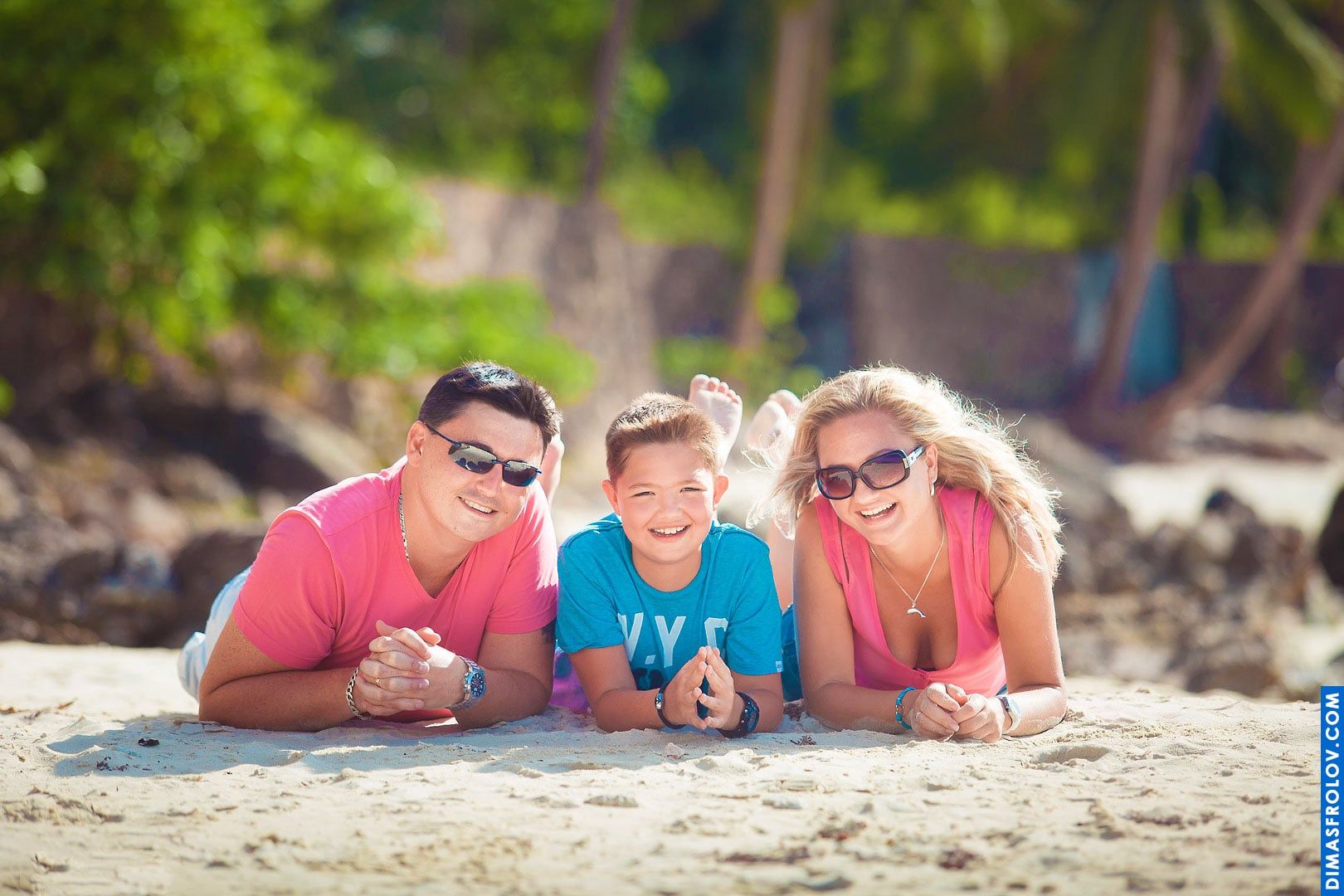 Retrato divertido na praia — pais com o filho deitados na areia, sorrindo juntos