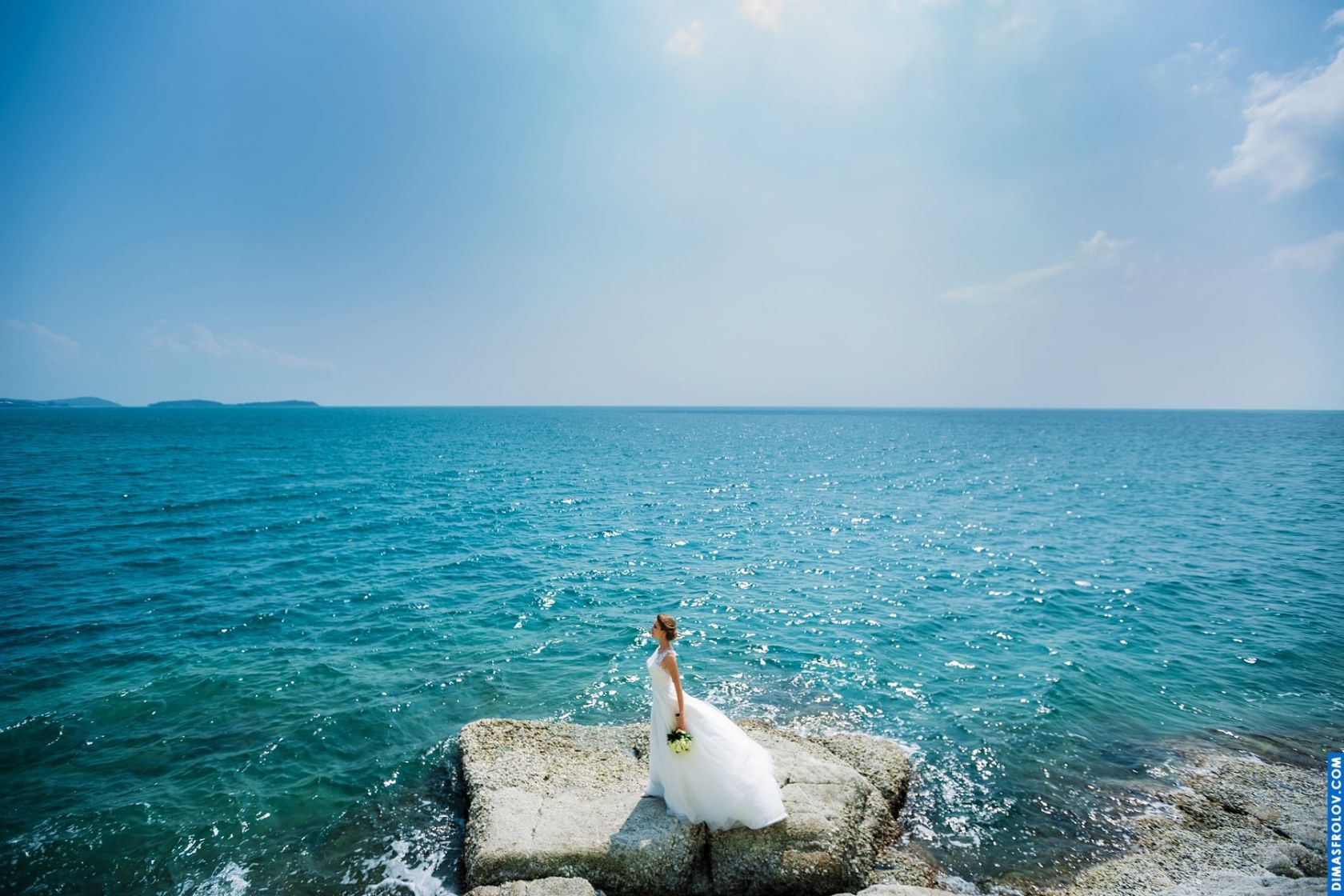 Bride standing on stone ledge in the sea — minimalist and powerful ocean shot
