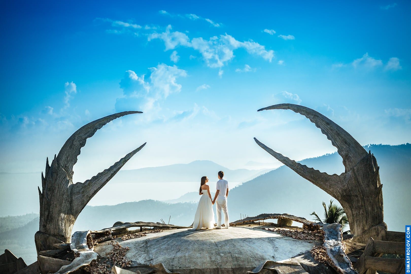 Wedding couple framed by giant crab claws overlooking the sea — bold destination shot