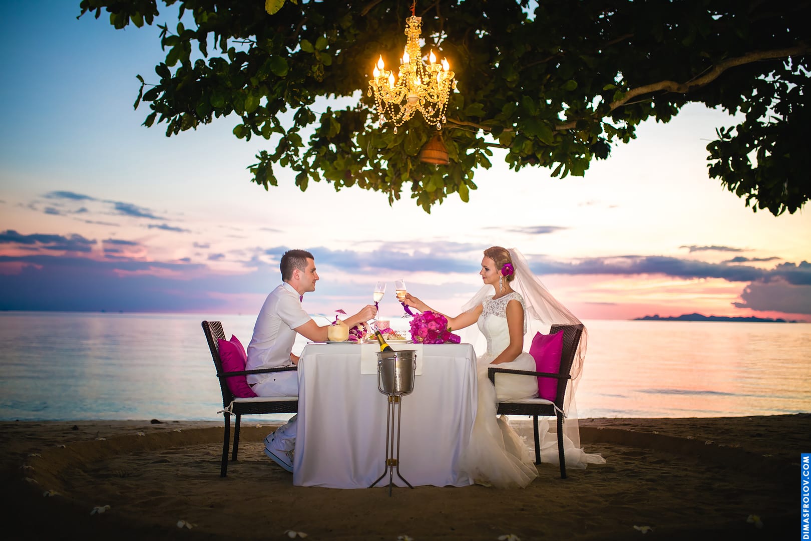 Elegant wedding dinner on the beach with chandelier and sunset view