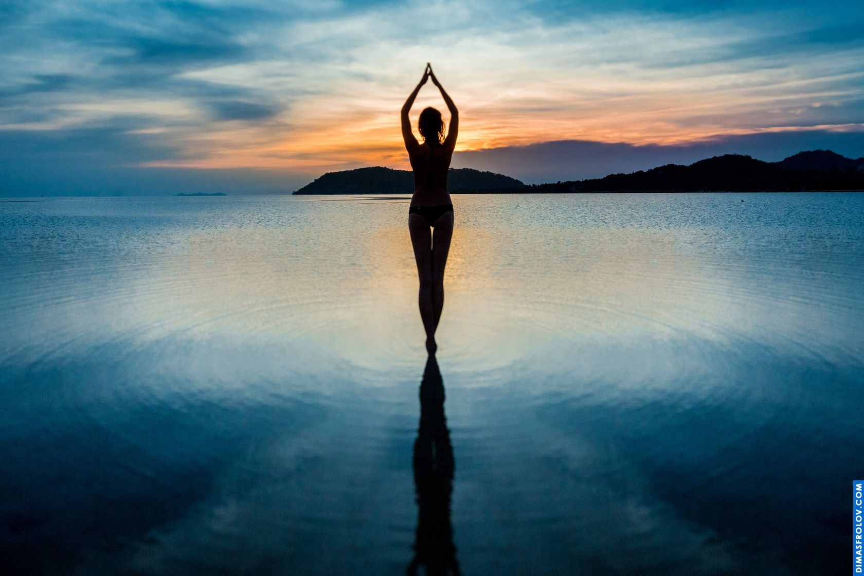 Artistic silhouette of a woman doing yoga pose on the water at sunrise