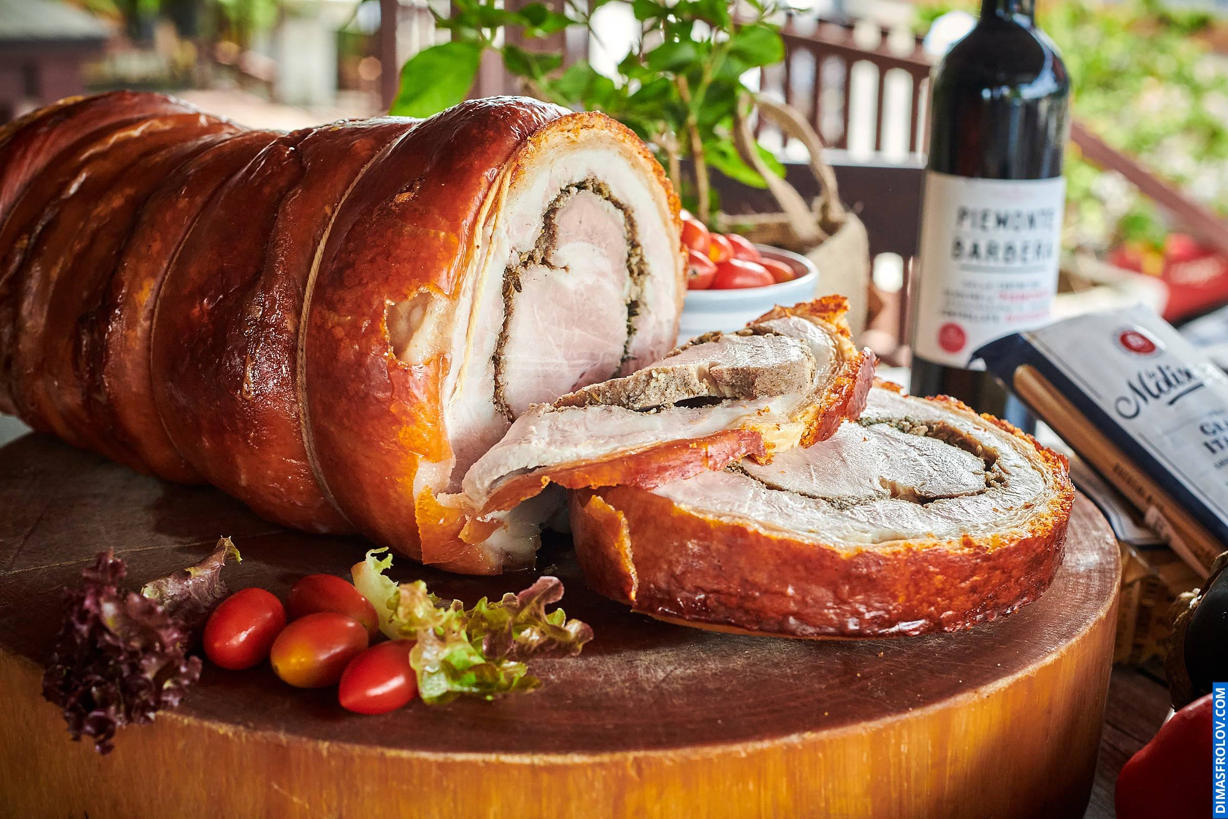Naturally lit, life-style shot of sliced porchetta on a wooden board with herbs and a bottle of wine, perfect for food bloggers and restaurants showcasing authentic dishes