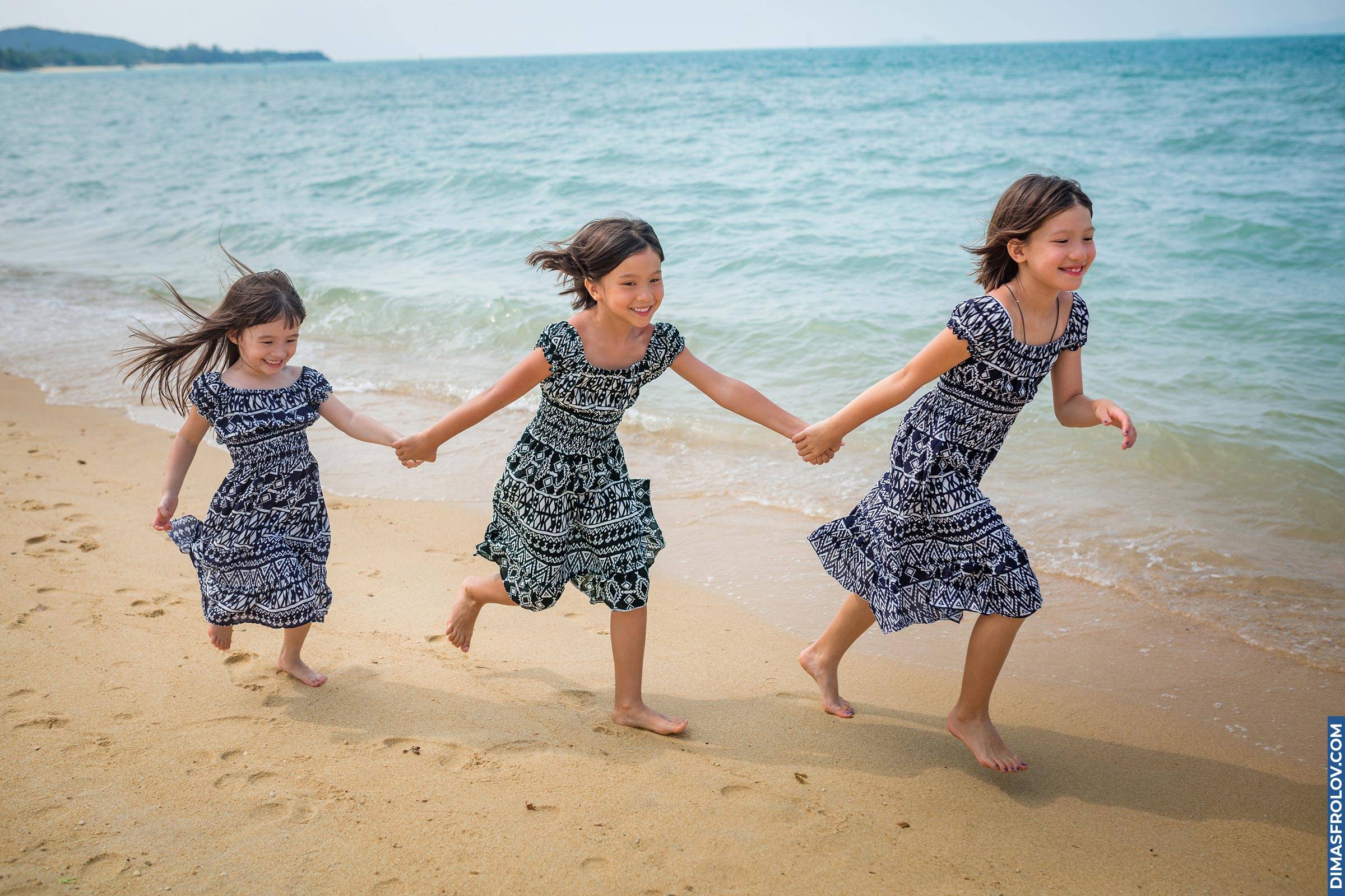 Three girls in matching dresses running and holding hands on the beach