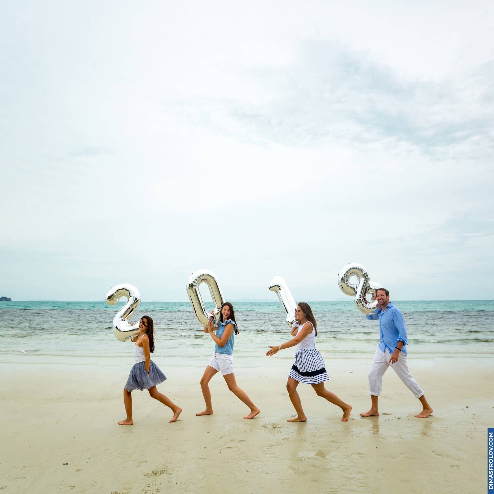 Family running on the beach holding silver number balloons
