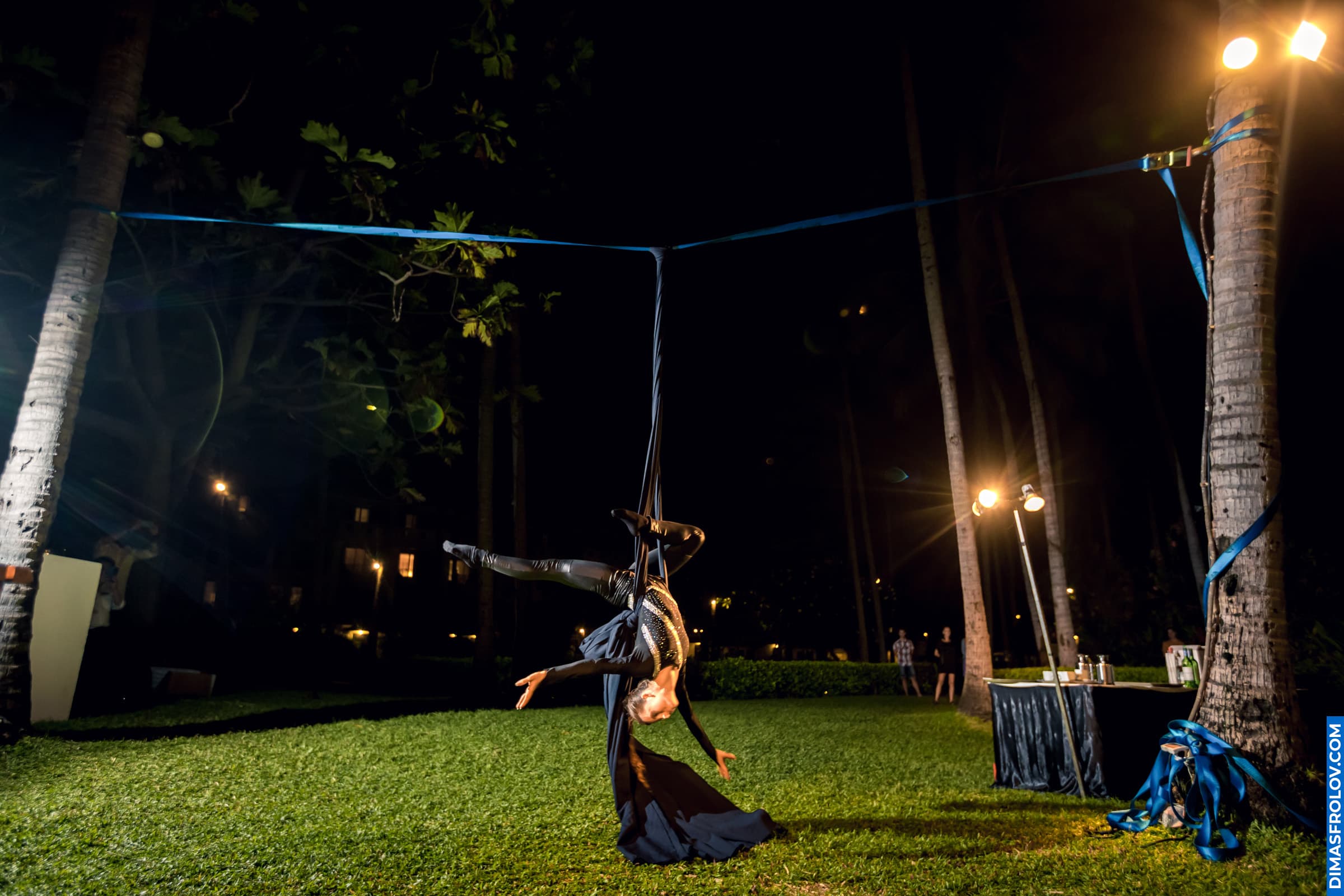 Nighttime aerial acrobat performance on slackline between palm trees