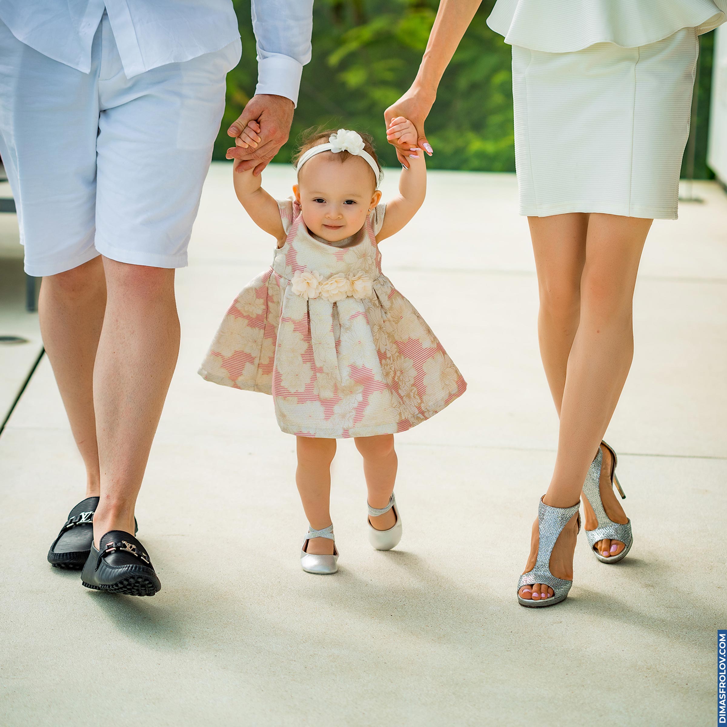 Toddler walking with help from parents holding her hands