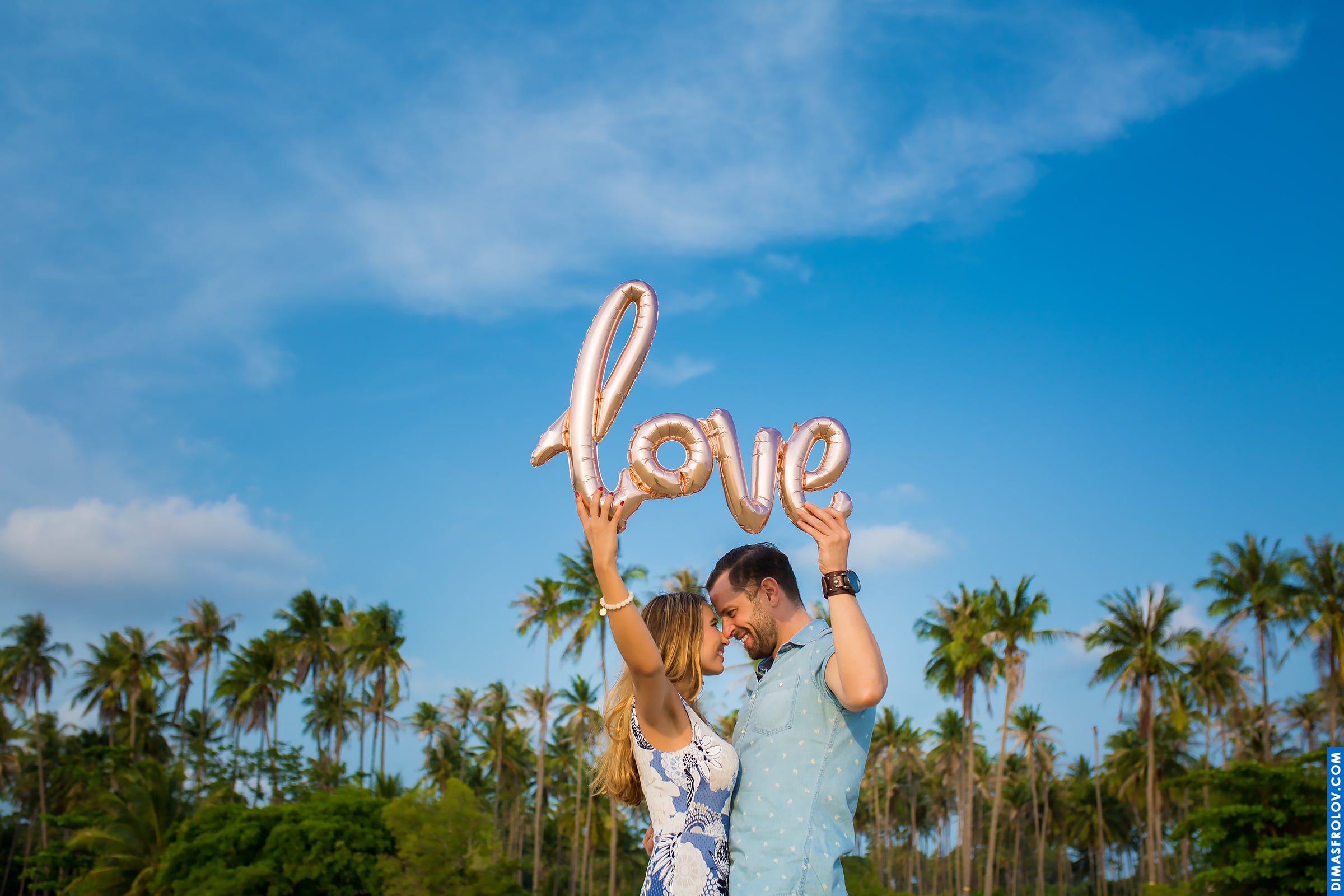 Fun engagement moment with LOVE balloon and palm trees in the background