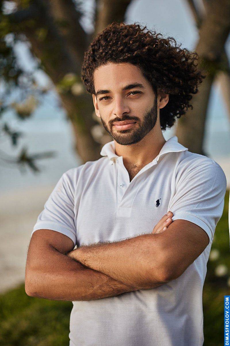 A relaxed seaside portrait: a man in a polo shirt stands with arms crossed during a calm photo shoot