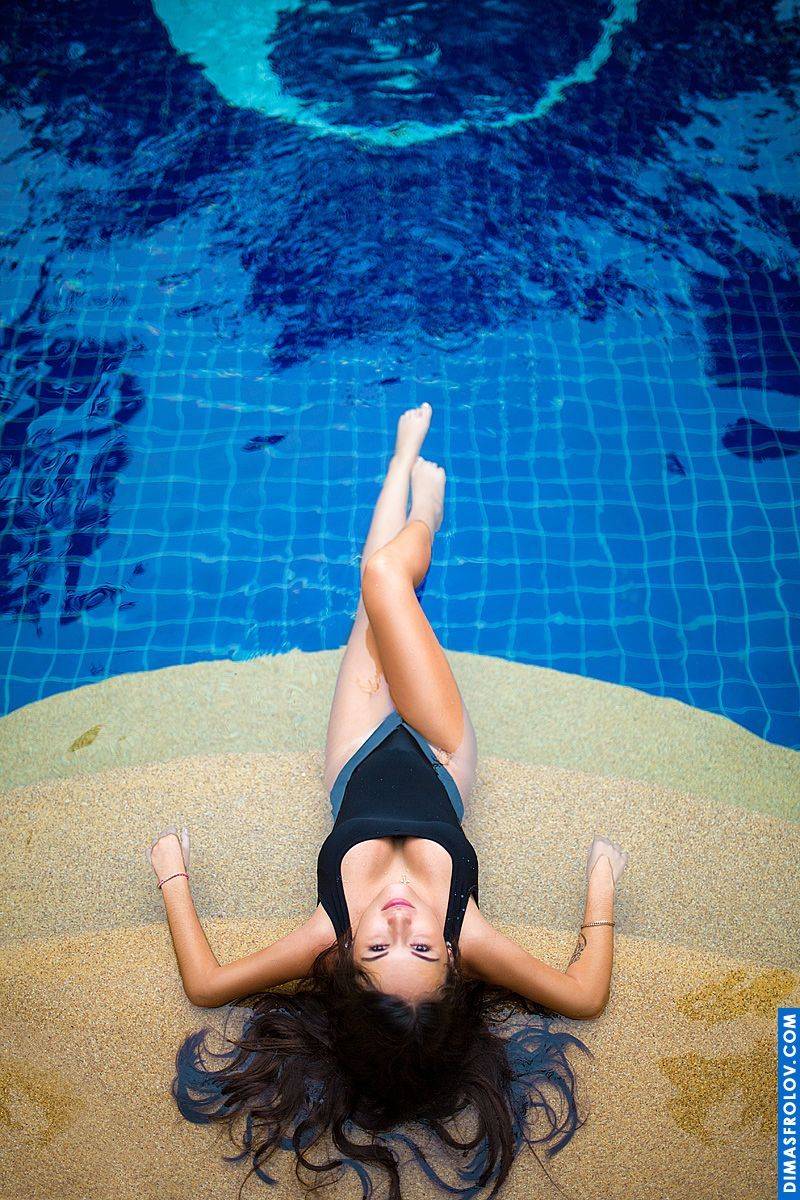 Poolside swimwear session with model in black monokini lying on the edge of blue water