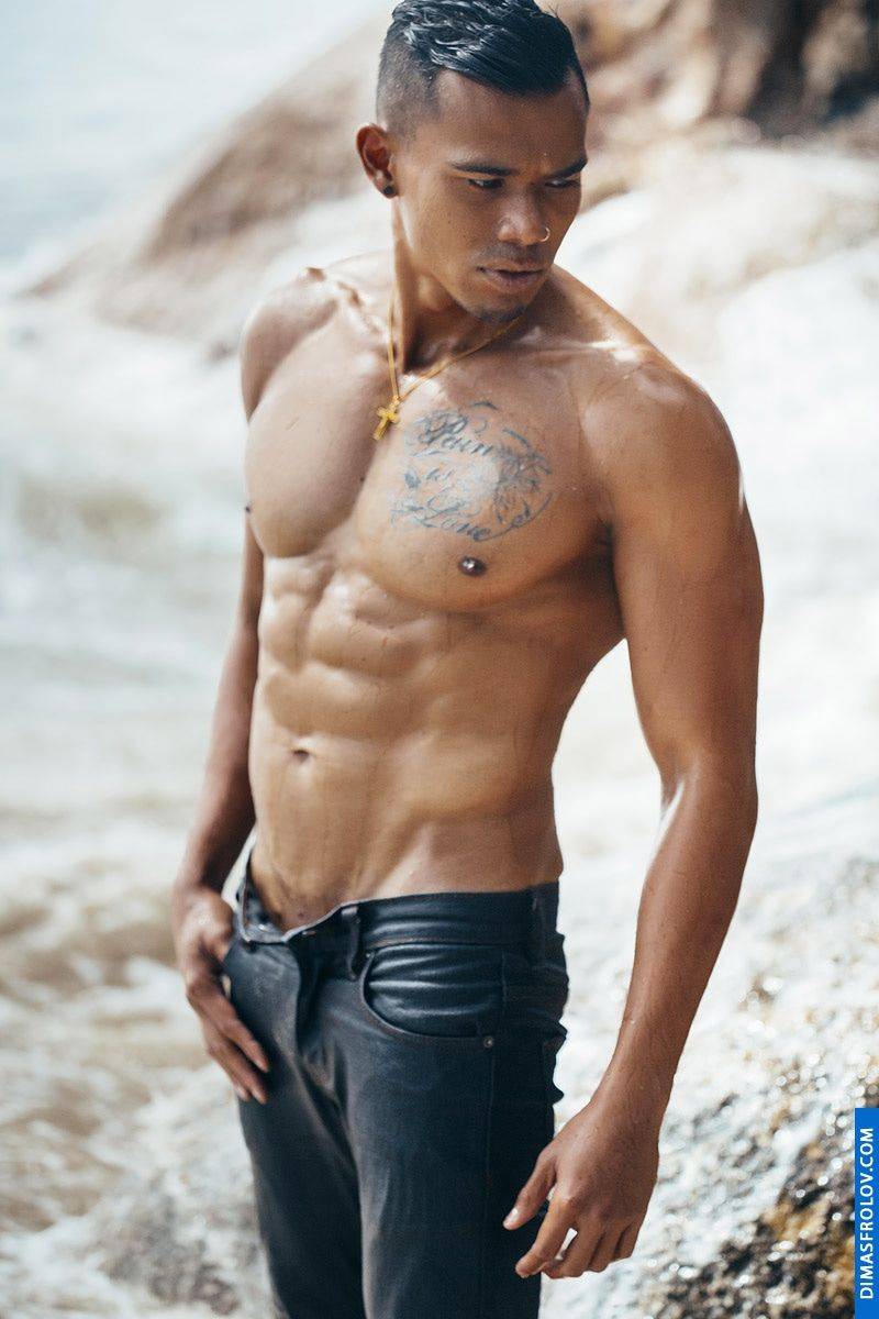 A striking beach portrait: a muscular man in jeans poses confidently during a dynamic photo shoot