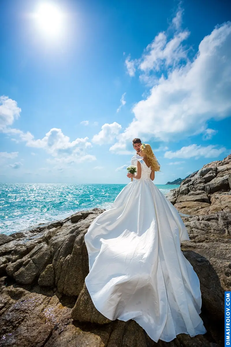 คู่บ่าวสาวยืนอยู่บนโขดหินริมทะเลใต้แสงแดด