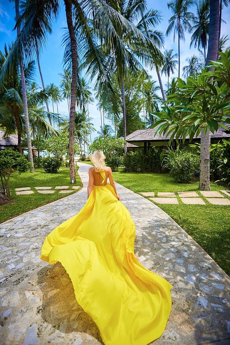 ภาพถ่ายด้านหลังของสาวผมบลอนด์ในชุดเดรสสีเหลืองกลางสวน