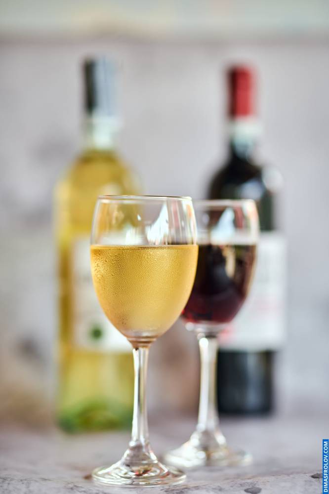 Life-style shot in natural light featuring glasses of white and red wine with blurred bottles in the background, ideal for wine bars and restaurants creating a real drink ambiance for their social media