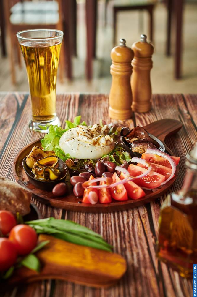 Naturally lit, life-style shot of a gourmet salad with olives and tomatoes, served with beer on a rustic wooden table, perfect for restaurants and pubs showcasing their menu in a real and appealing way