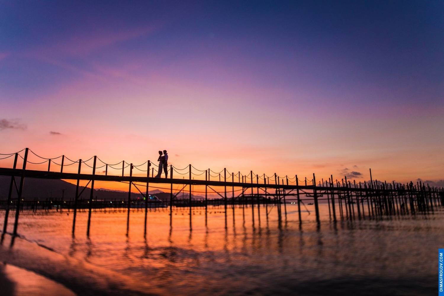 Sunset silhouette on the pier — romantic wedding shot with glowing reflections