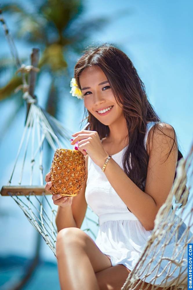 Tropical portrait of a cheerful young woman enjoying pineapple in a hammock