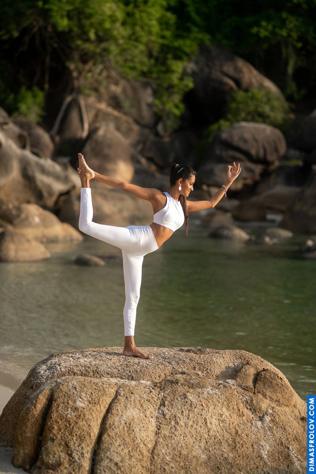 Graceful balance in nature: woman in dancer pose on a rock by the water